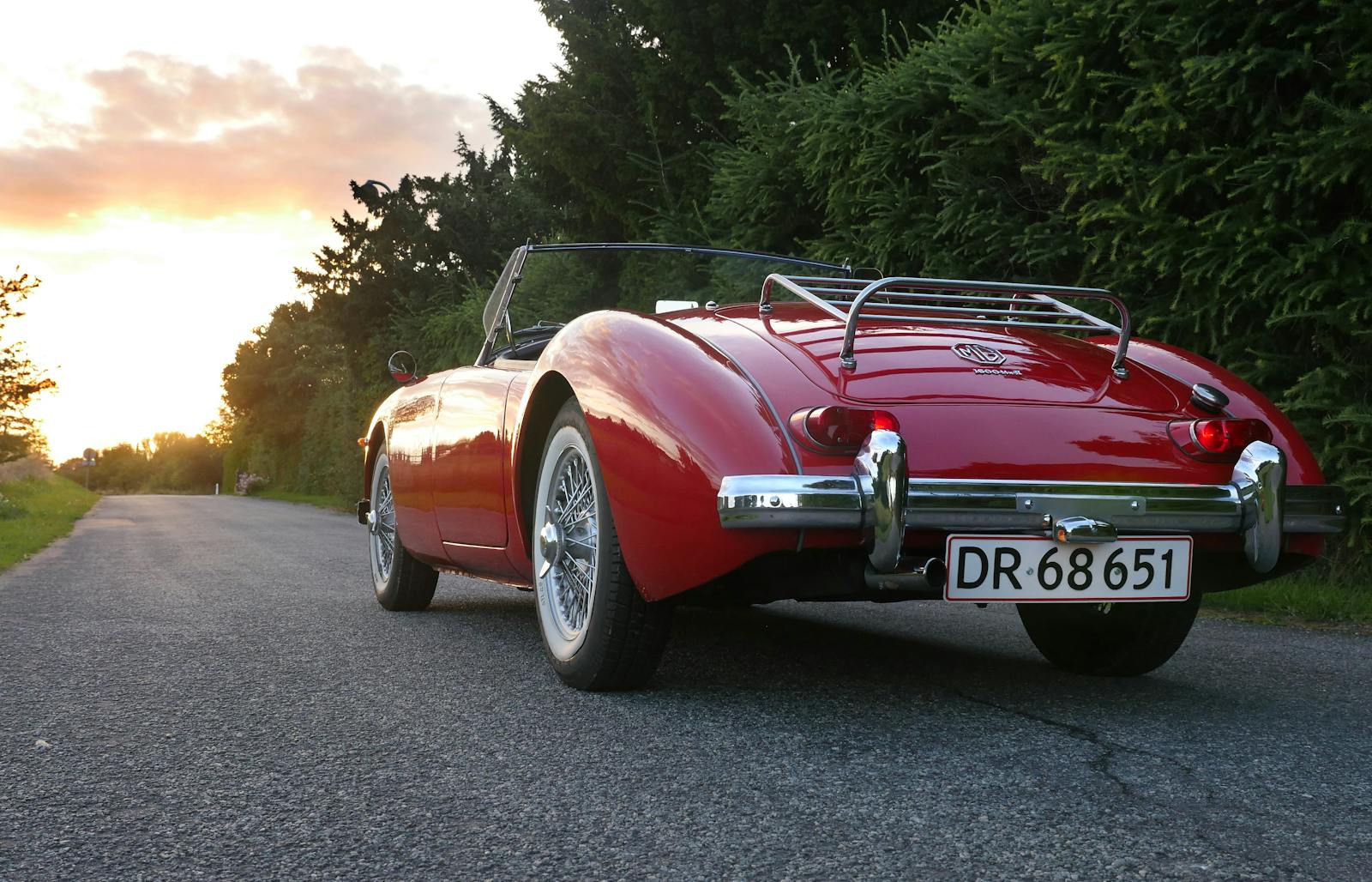 classic car classic red convertible parked on a scenic road at sunset, showcasing luxury and style.